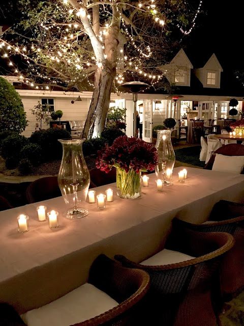 a long table with lit candles and flowers on it in front of a white house