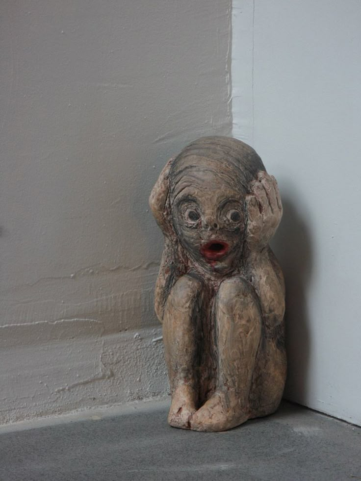 a statue of a baby sitting on the ground next to a white wall and cement floor