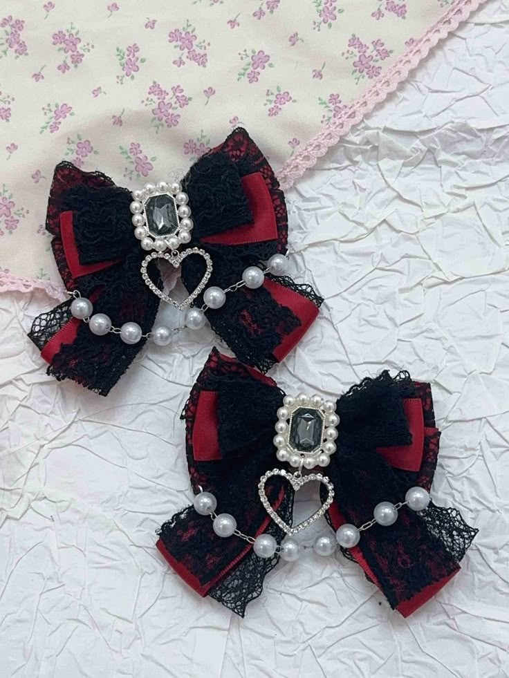 two black and red hair bows with pearls on them sitting on a white surface next to a pink flowered cloth