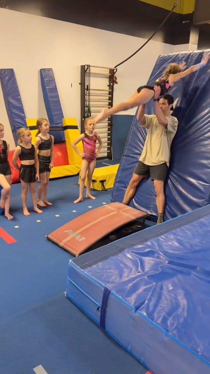 a group of children standing on top of a blue trampoline in a gym