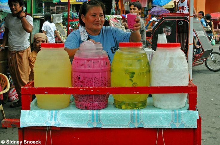 a woman standing behind a cart filled with different colored jars and containers on top of it