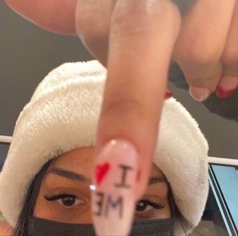 a woman wearing a white hat and holding up her finger with the word i love me written on it