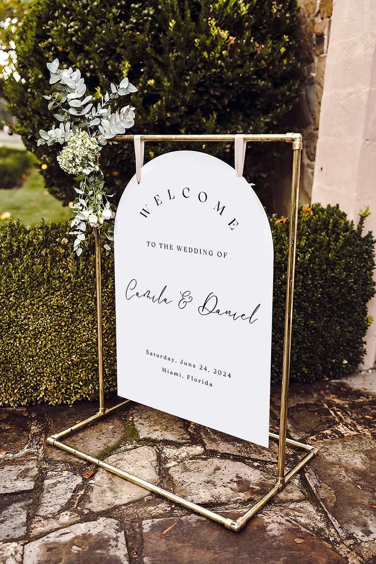 a welcome sign with flowers on it sitting in front of a bush