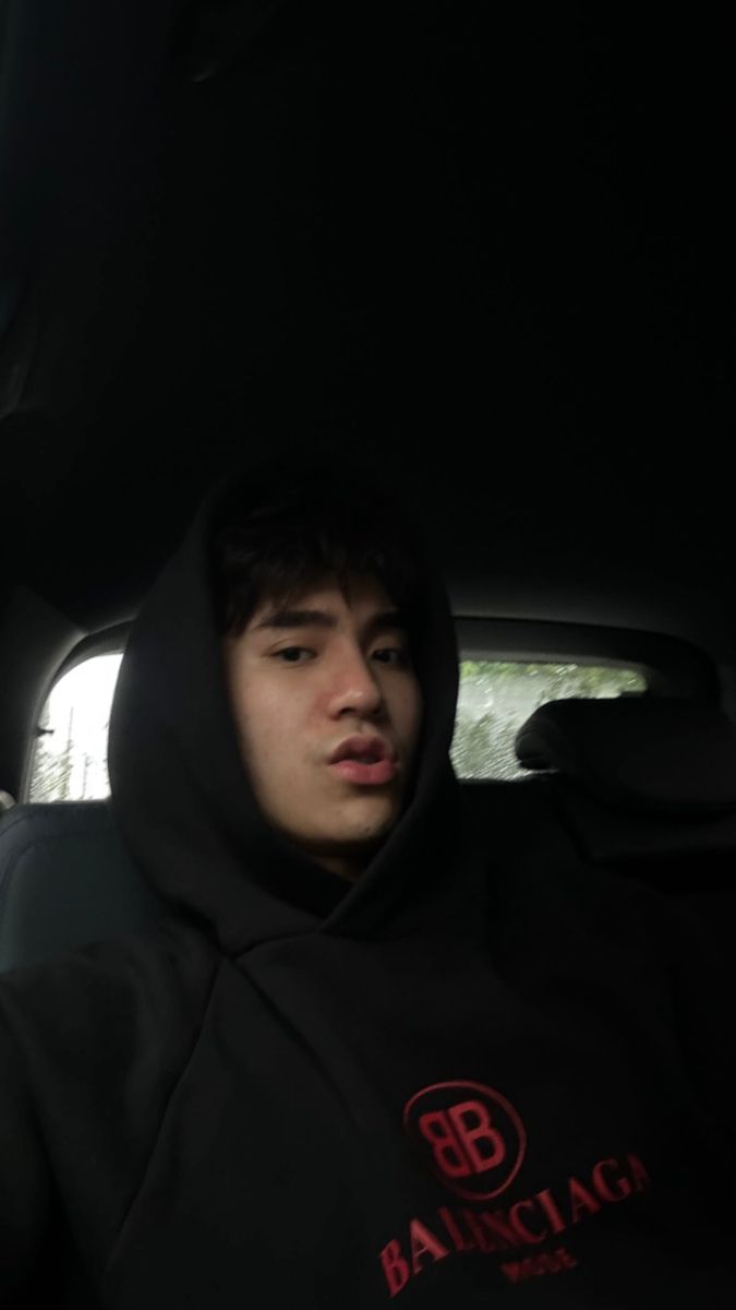 a young man sitting in the back seat of a car wearing a black hoodie