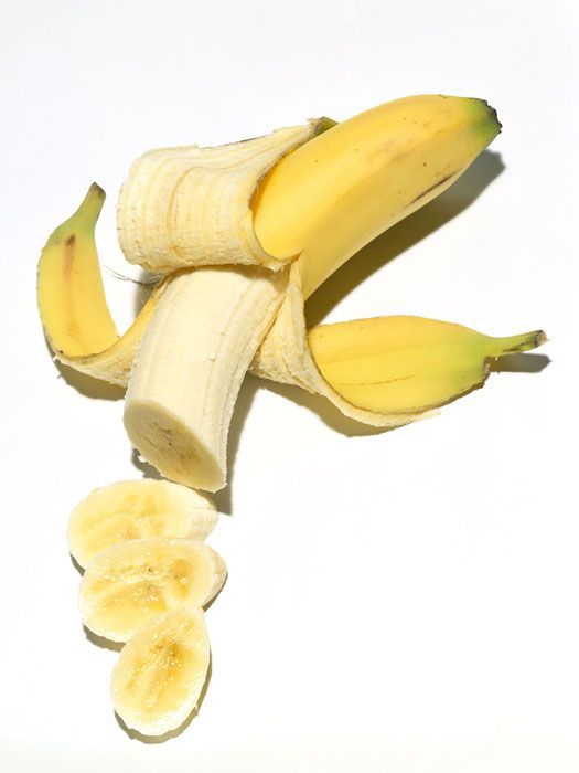 two peeled bananas and one cut in half on a white surface with the peels still attached