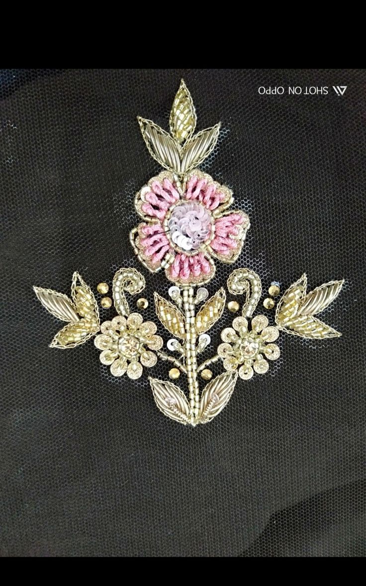 a pink and gold brooch sitting on top of a piece of cloth next to a black background