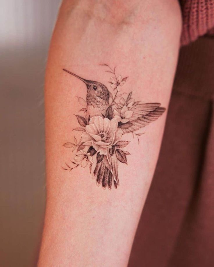 a humming bird with flowers on its arm