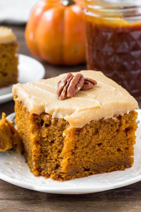 a slice of pumpkin cake with frosting and pecans in the background on a white plate