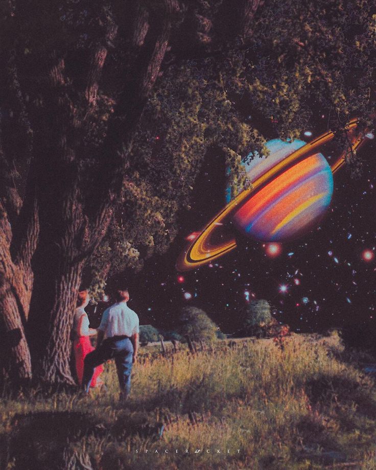 two people are standing in the grass looking at an image of saturn and its rings