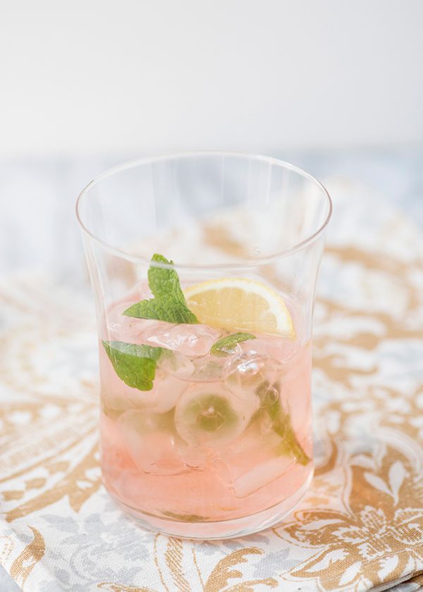 a close up of a drink in a glass with ice and lemon slices on the rim