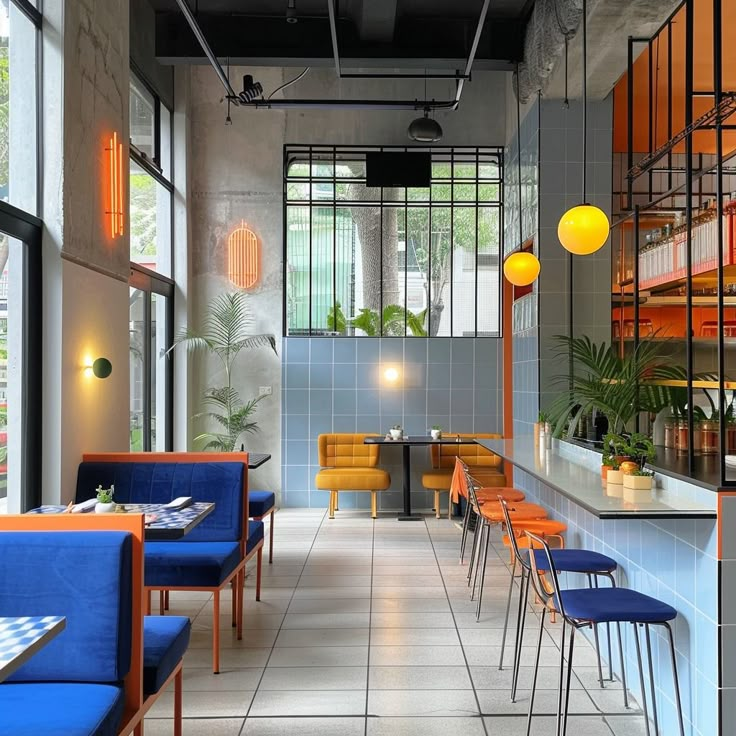 an empty restaurant with blue chairs and yellow lights hanging from the ceiling, along with orange accents