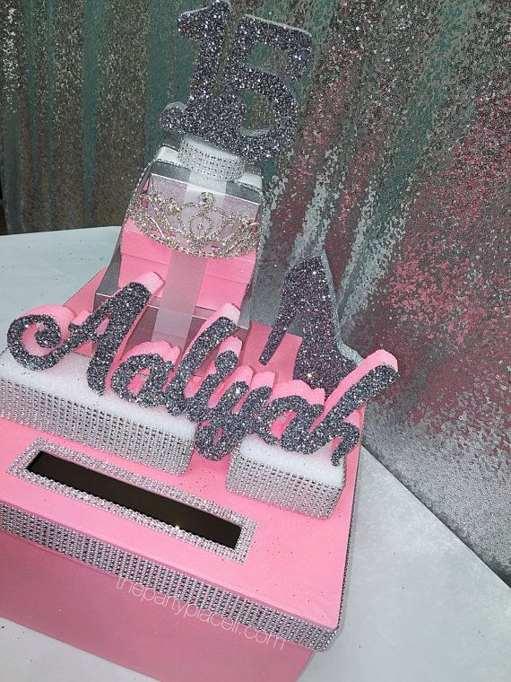 a pink and silver cake sitting on top of a table next to a wall with glitter letters