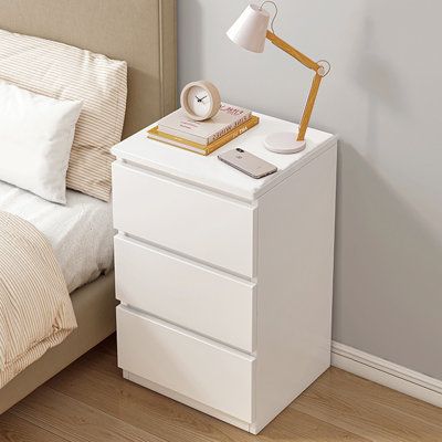 a white night stand with two drawers and a lamp next to it on a wooden floor