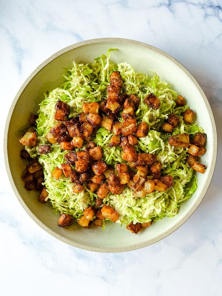 a white bowl filled with lettuce and meat on top of a marble counter