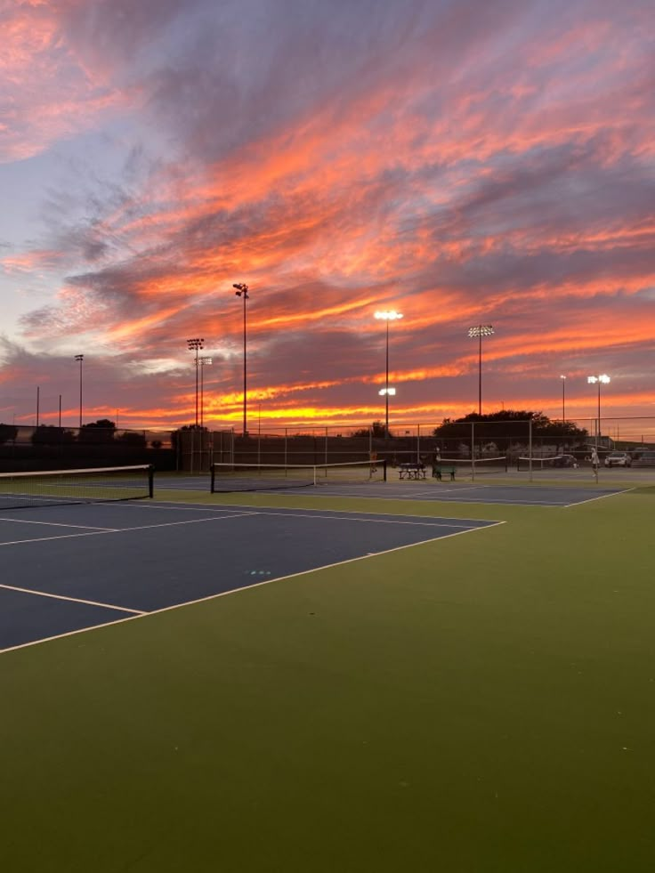 a tennis court with the sun setting in the background