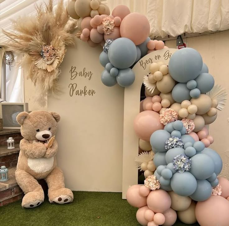 a teddy bear sitting next to a giant balloon arch