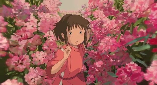 a girl standing in front of pink flowers with her hand on her chest and looking at the camera