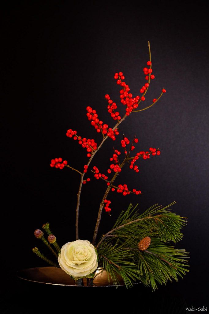 a vase filled with flowers and greenery on top of a wooden table next to a black wall