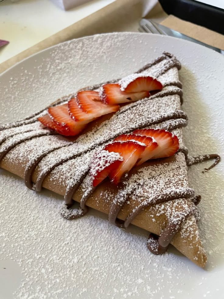 some strawberries are sitting on top of a piece of chocolate covered pastry with powdered sugar