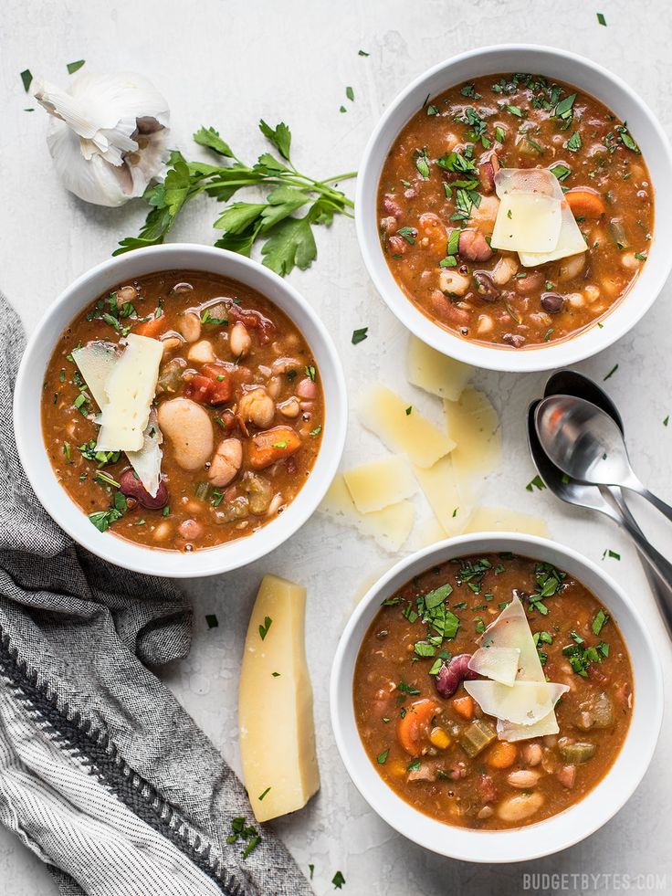 three bowls of vegetarian bean soup with parmesan cheese and herbs on the side