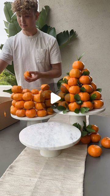 a young man standing in front of three tiered trays filled with oranges