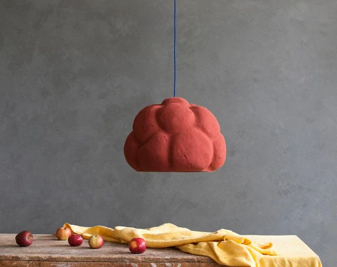 a red cloud shaped object hanging from a blue string next to fruit on a table