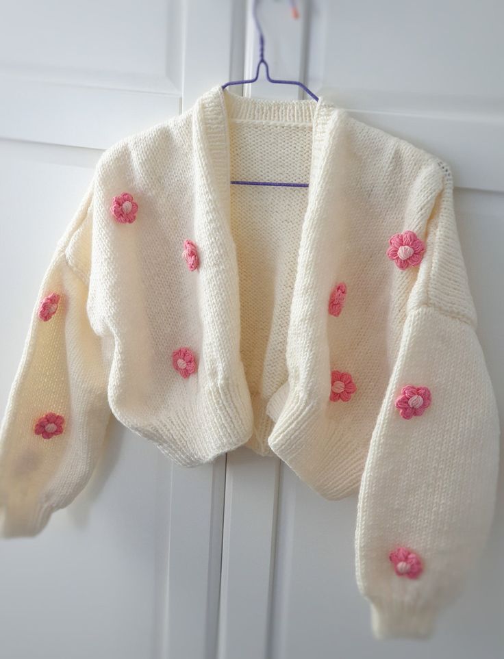 a white sweater with pink flowers on it hanging from a hook in front of a door