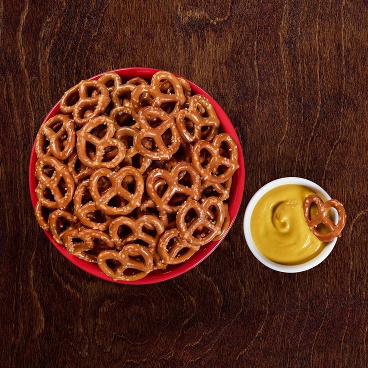 a red plate with pretzels and mustard on it next to a bowl of dip