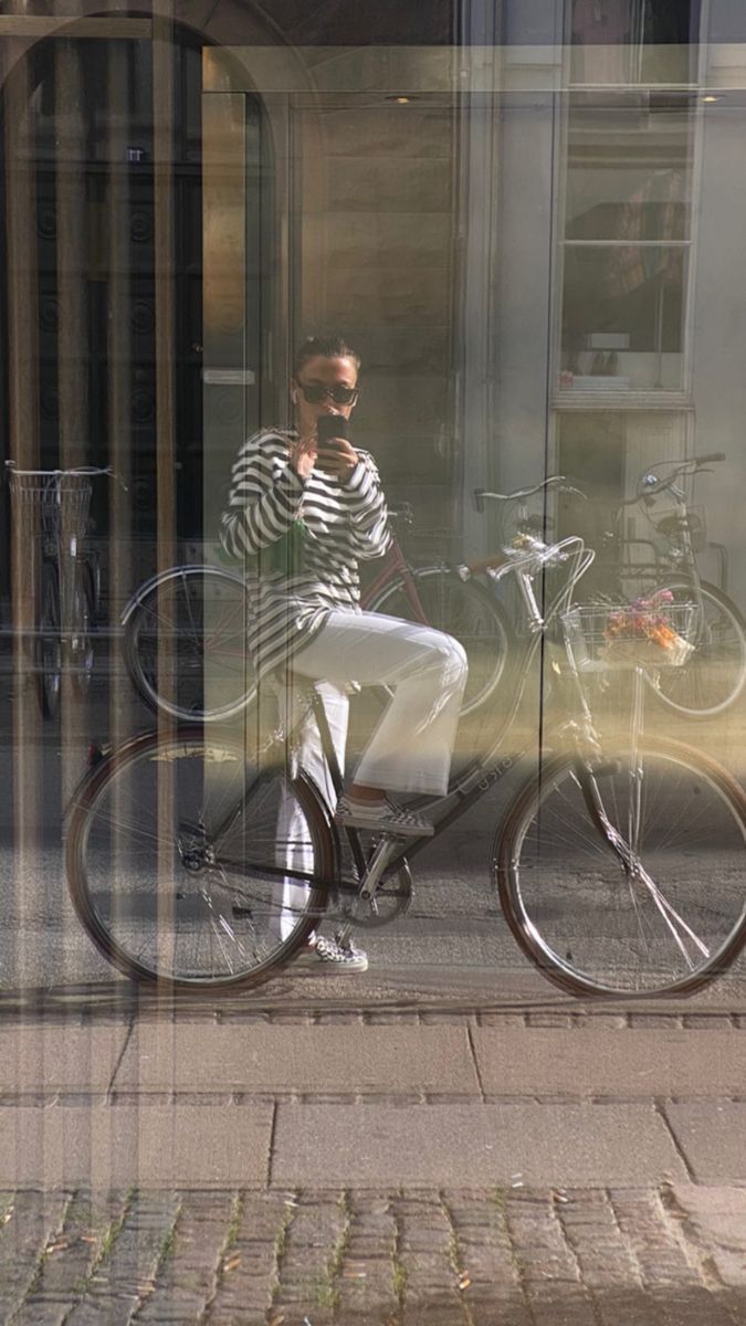 a man sitting on a bike in front of a store window taking a selfie with his cell phone