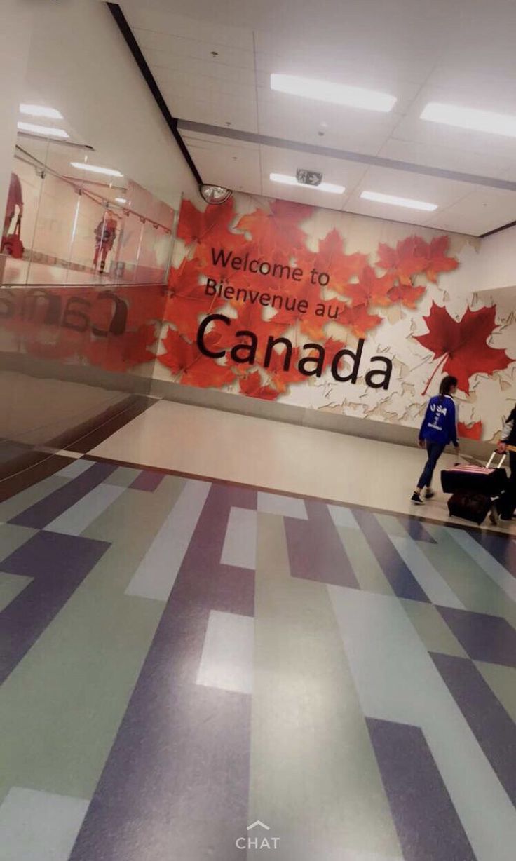 people are walking through an airport lobby with canadian flag on the wall and welcome sign