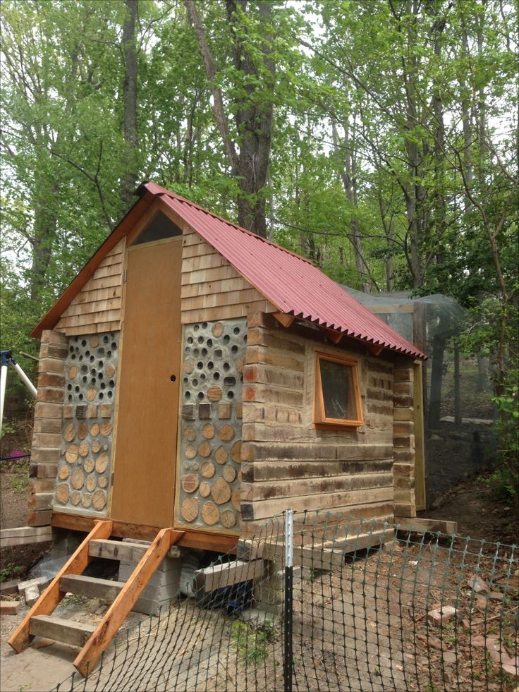 a small wooden cabin in the woods with a red metal roof and stairs leading up to it