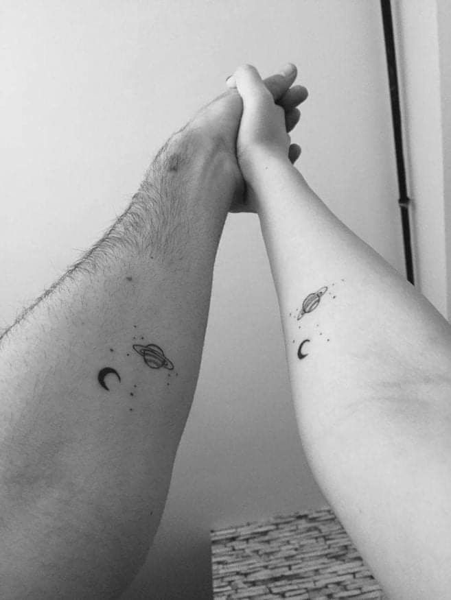 two people are holding hands with the moon and planets tattooed on their arms, both of them