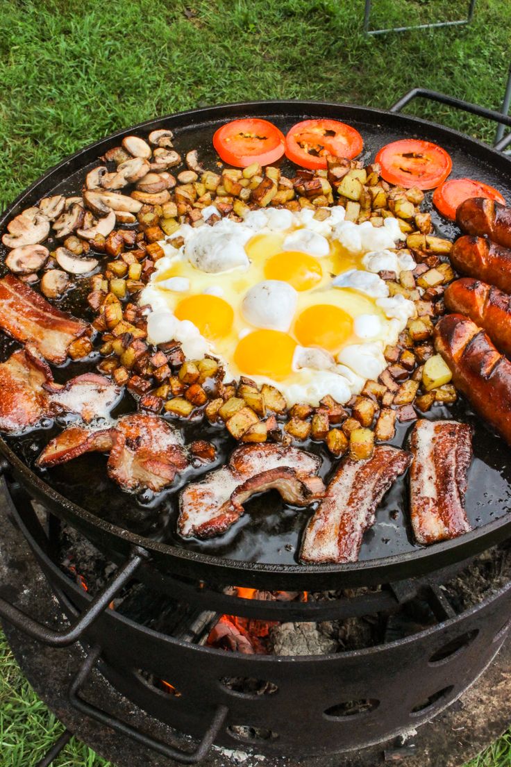 an outdoor grill with eggs, sausages and other foods cooking on top of it