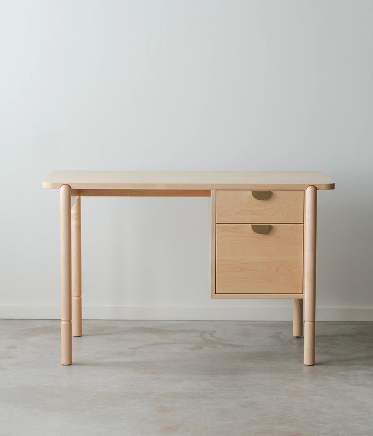 a wooden desk with two drawers on the bottom and one drawer at the top, in front of a white wall