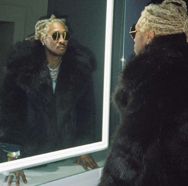 a man with dreadlocks is looking at himself in the mirror while wearing a fur coat