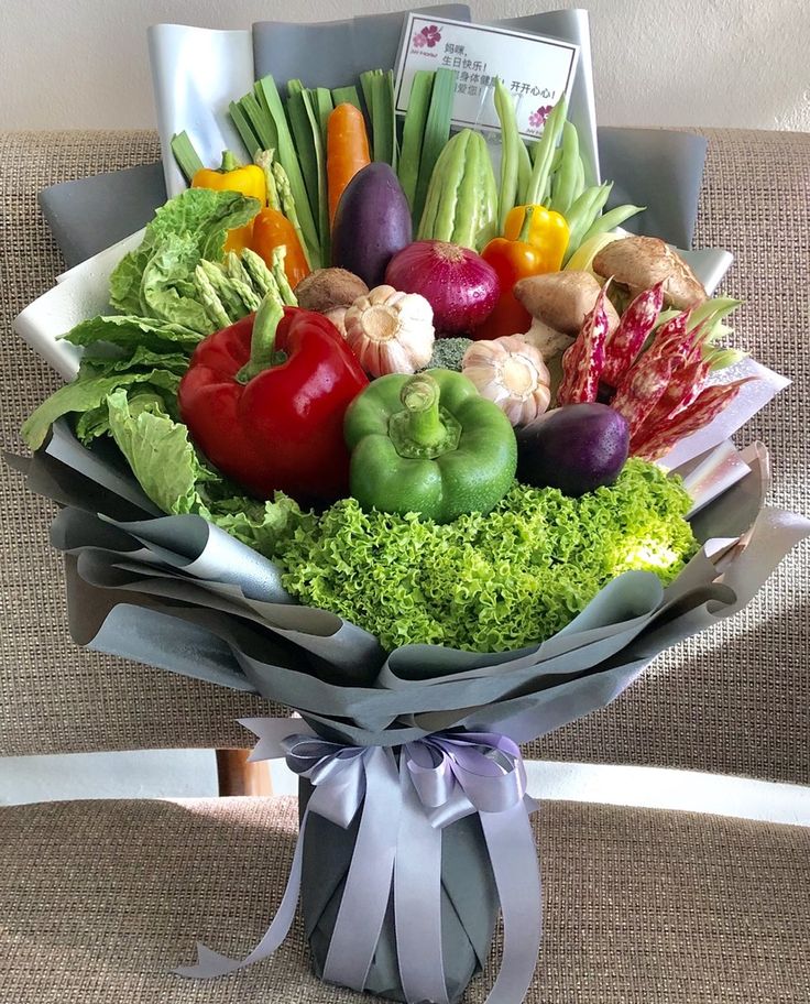 a bouquet of fresh fruits and vegetables is wrapped in gray paper with a ribbon around it