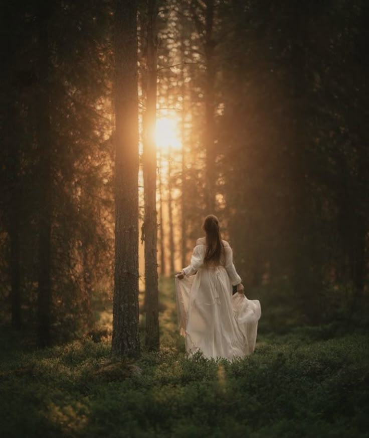 a woman is walking through the woods at sunset