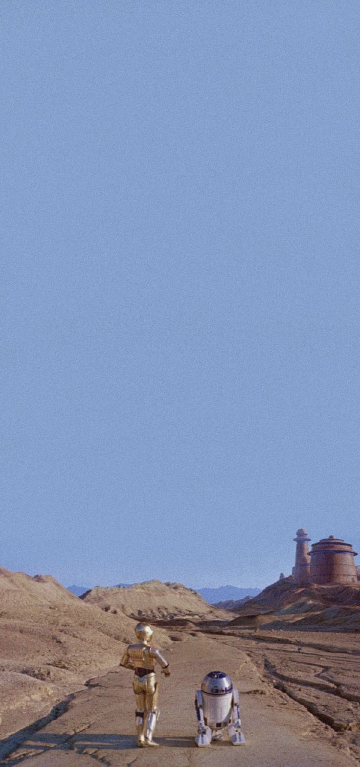 two people walking down a dirt road in the middle of desert with an airplane flying overhead