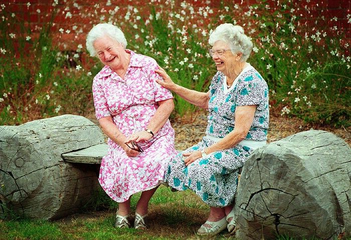 two older women sitting next to each other on top of large rocks in the grass