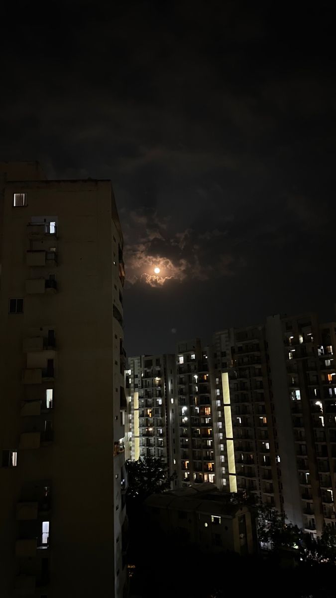 the night sky is dark and cloudy, with buildings in the foreground lit up by bright lights