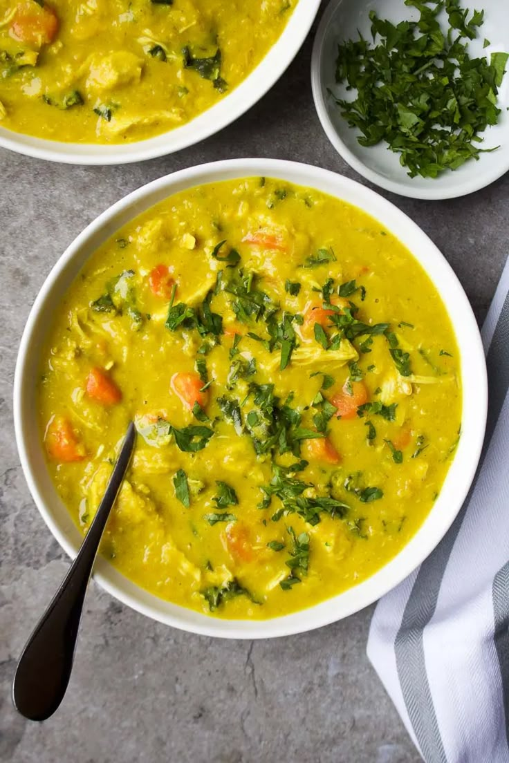 two white bowls filled with yellow soup and garnished with parsley on the side