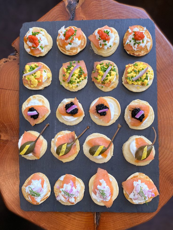 an assortment of small pastries are displayed on a black tray with wood slices around them