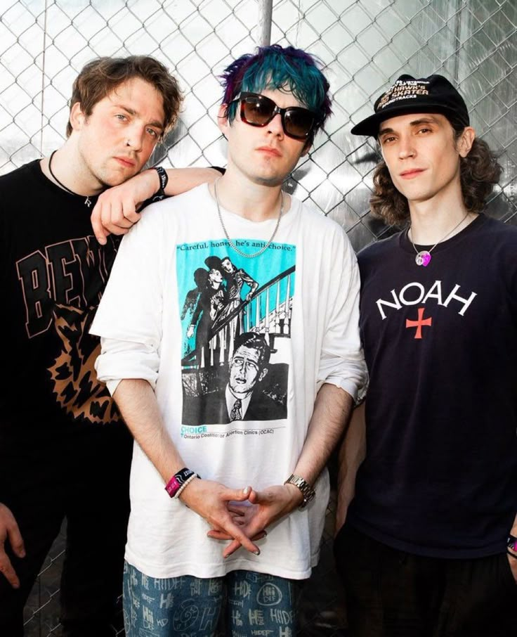 three young men standing next to each other in front of a chain link fence with their arms around one another