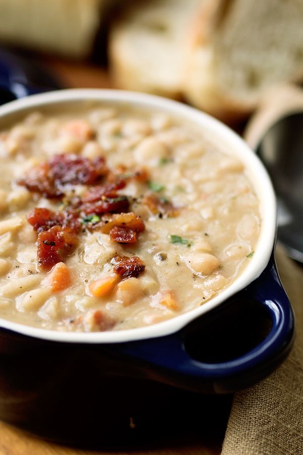 a bowl of soup with bacon and bread in the background