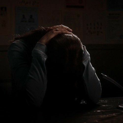 a person sitting at a desk with their head on his hands and the dark room behind them