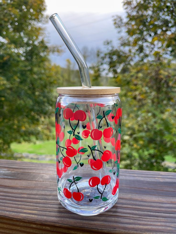 a glass cup with a straw in it sitting on a wooden table next to trees