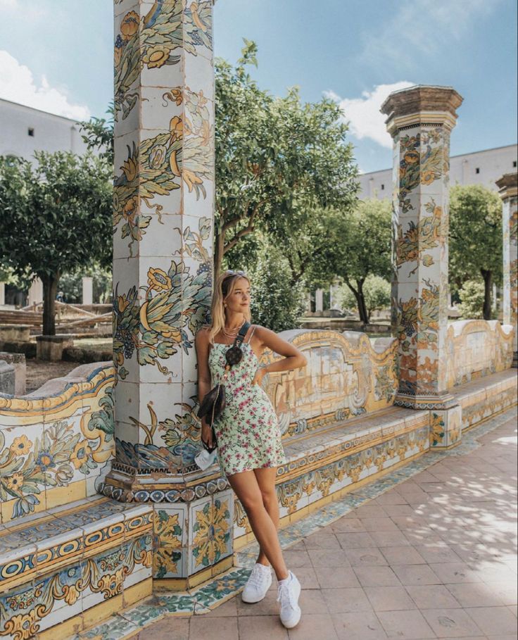 a woman leaning against a pillar in front of an ornate wall with flowers on it