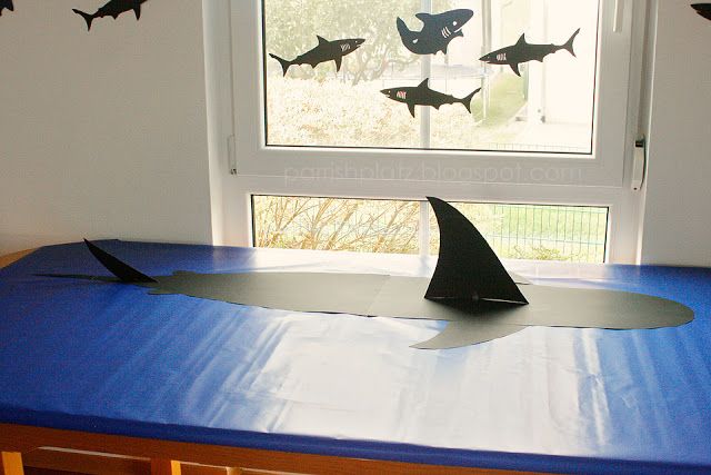 a blue table topped with a paper boat and shark silhouettes hanging from the window