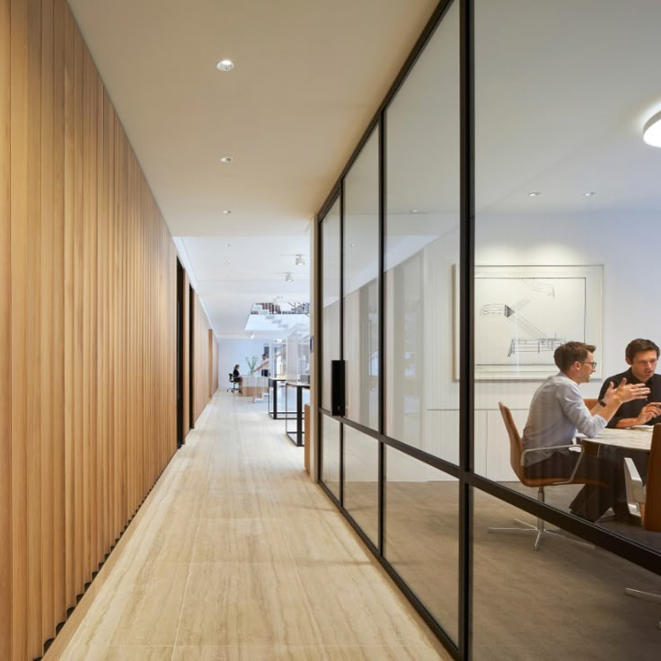 two people are sitting at a table in the middle of a long hallway with wood paneling