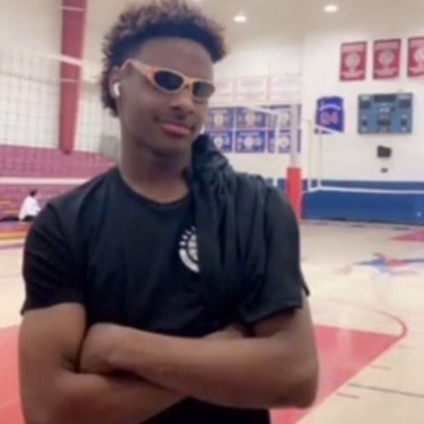 a young man with his arms crossed standing in front of a basketball court wearing sunglasses